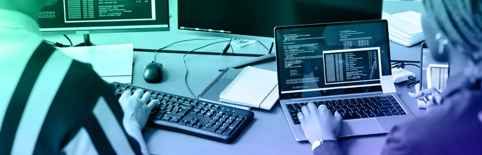 Software engineers reviewing code on a laptop and desktop monitors